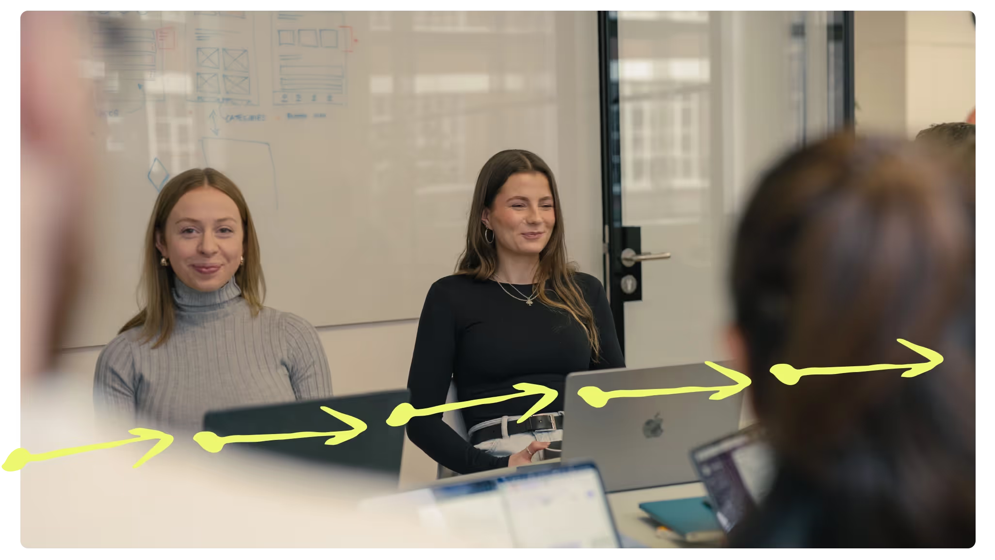 Two colleagues smiling in a meeting, with a hand-drawn yellow arrow line across the photo