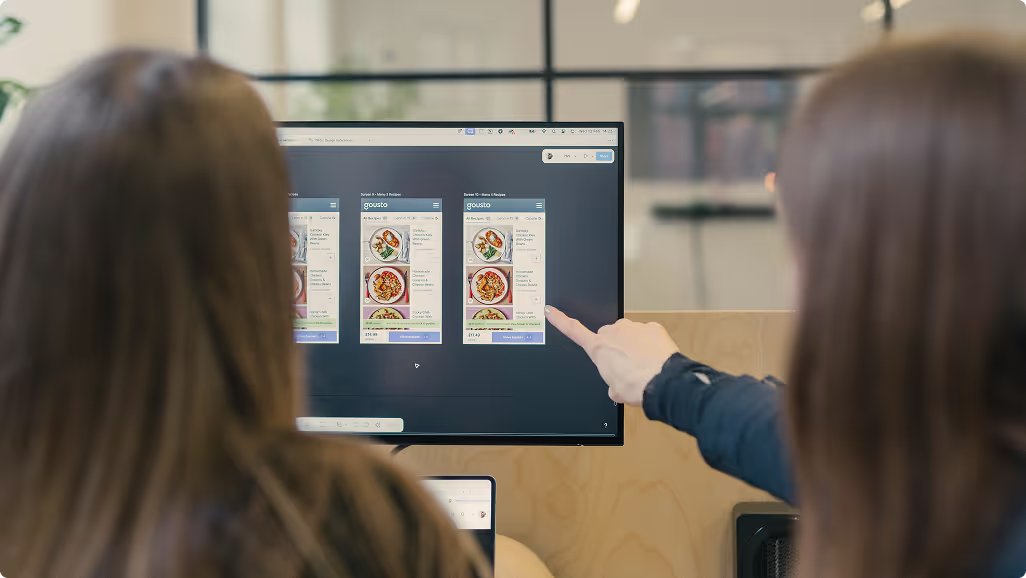 Two people pointing at mobile screen designs on a monitor
