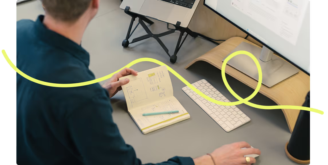 Person at a desk flicking through a notebook, with a looping yellow line drawn over the photo