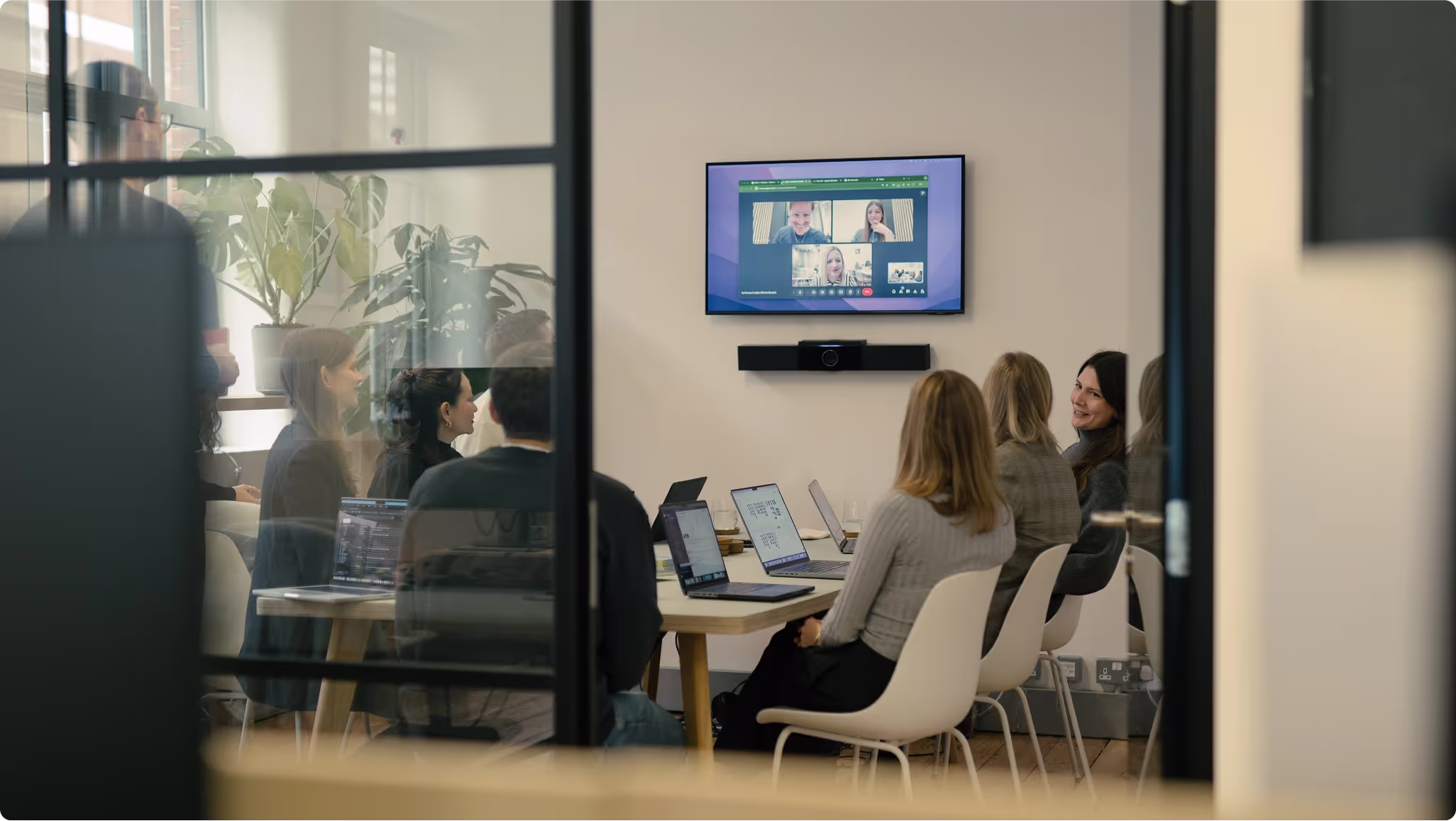 Team meeting around a table with remote colleagues on a video call, seen through glass