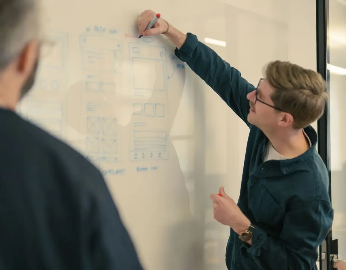 Designer sketching wireframes on a whiteboard as colleagues watch