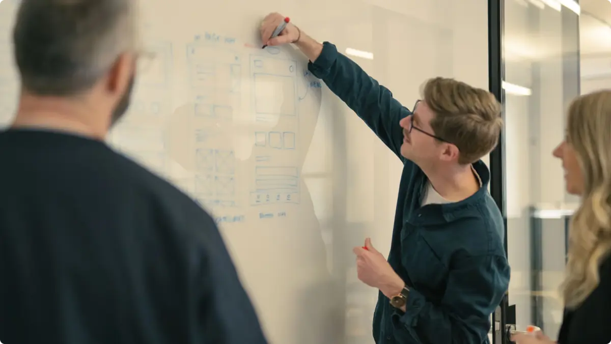 Designer sketching wireframes on a whiteboard as colleagues watch