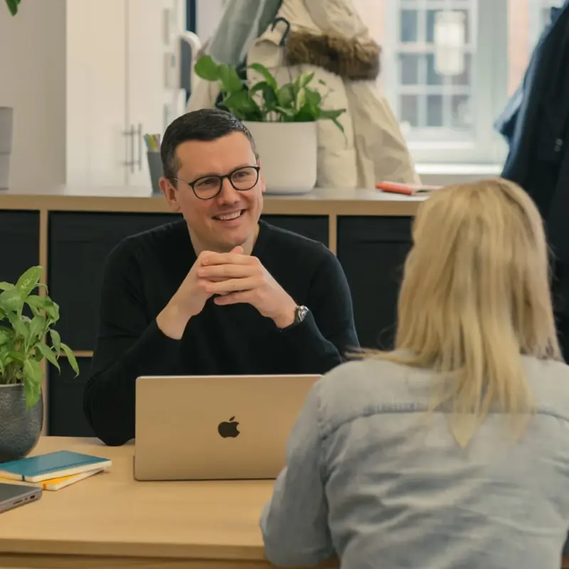 Team member smiling across a desk at a colleague during a conversation in the studio