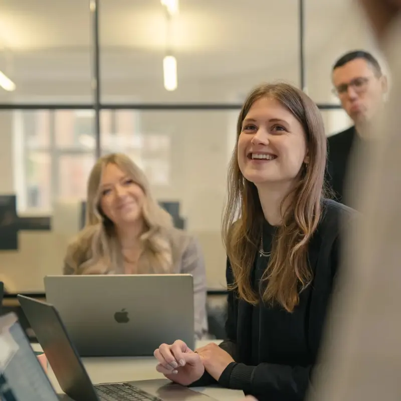 Two team members smiling at their laptops during a studio meeting