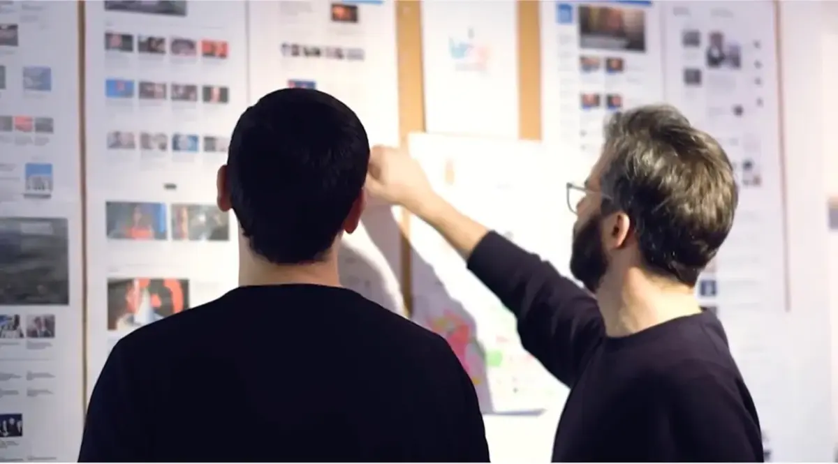 Two people reviewing printed web page designs pinned to a wall