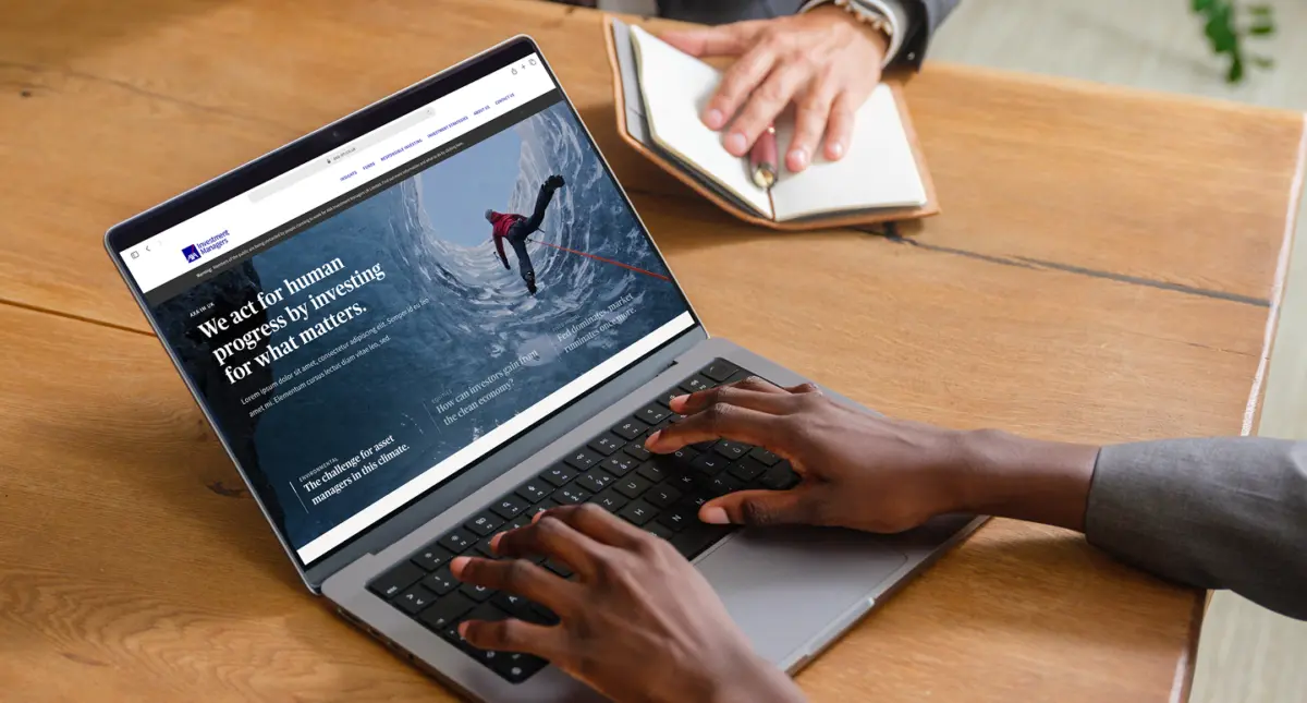 Person typing on a laptop showing the AXA IM homepage, 'We act for human progress by investing for what matters'