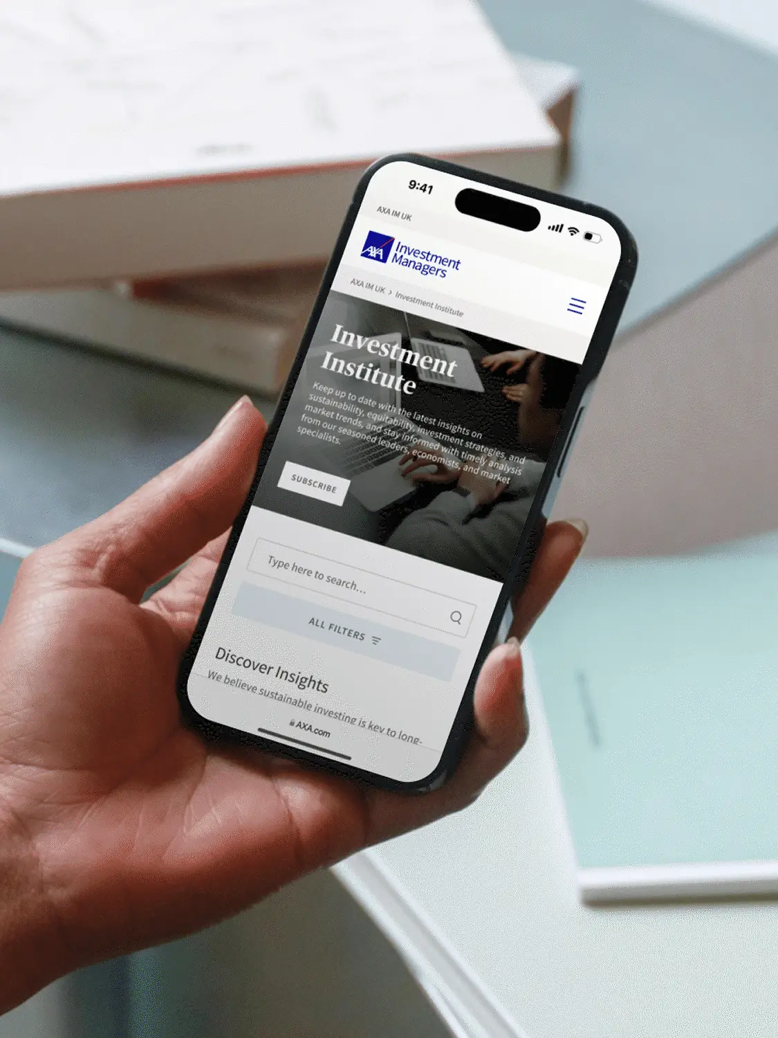 Hand holding a phone showing the AXA IM Investment Institute page