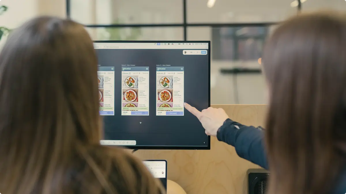 Two people pointing at Gousto menu screen variants on a monitor