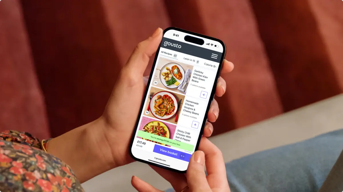 Hands holding a phone showing the Gousto recipe menu with a 'View basket' button