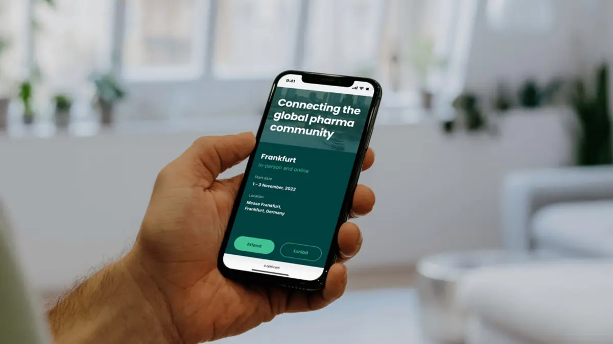 Hand holding a phone showing the CPHI Frankfurt event page, 'Connecting the global pharma community'