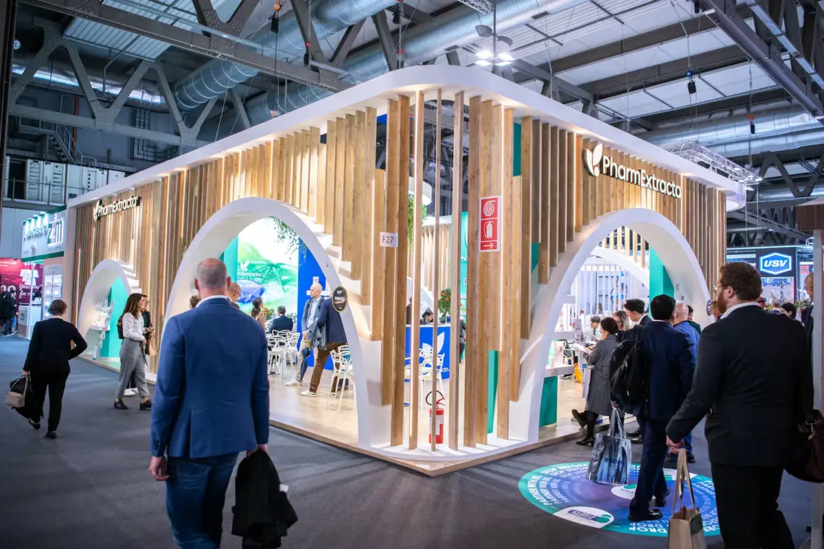 Visitors walking past a large exhibition stand in a busy trade show hall