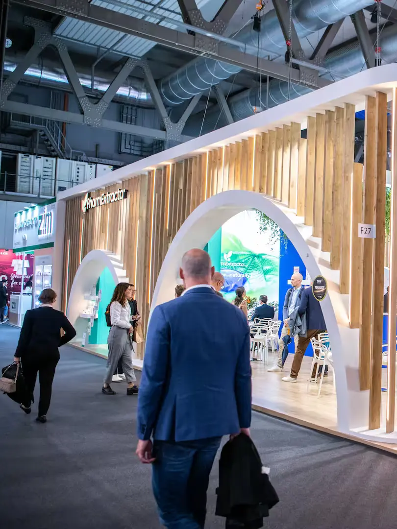 Visitors walking past a large exhibition stand in a busy trade show hall