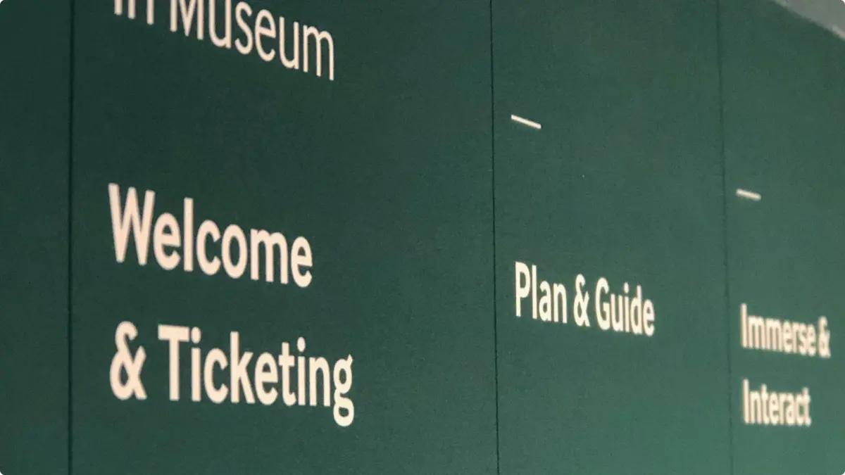Green museum wall with the headings 'Welcome & Ticketing', 'Plan & Guide' and 'Immerse & Interact'