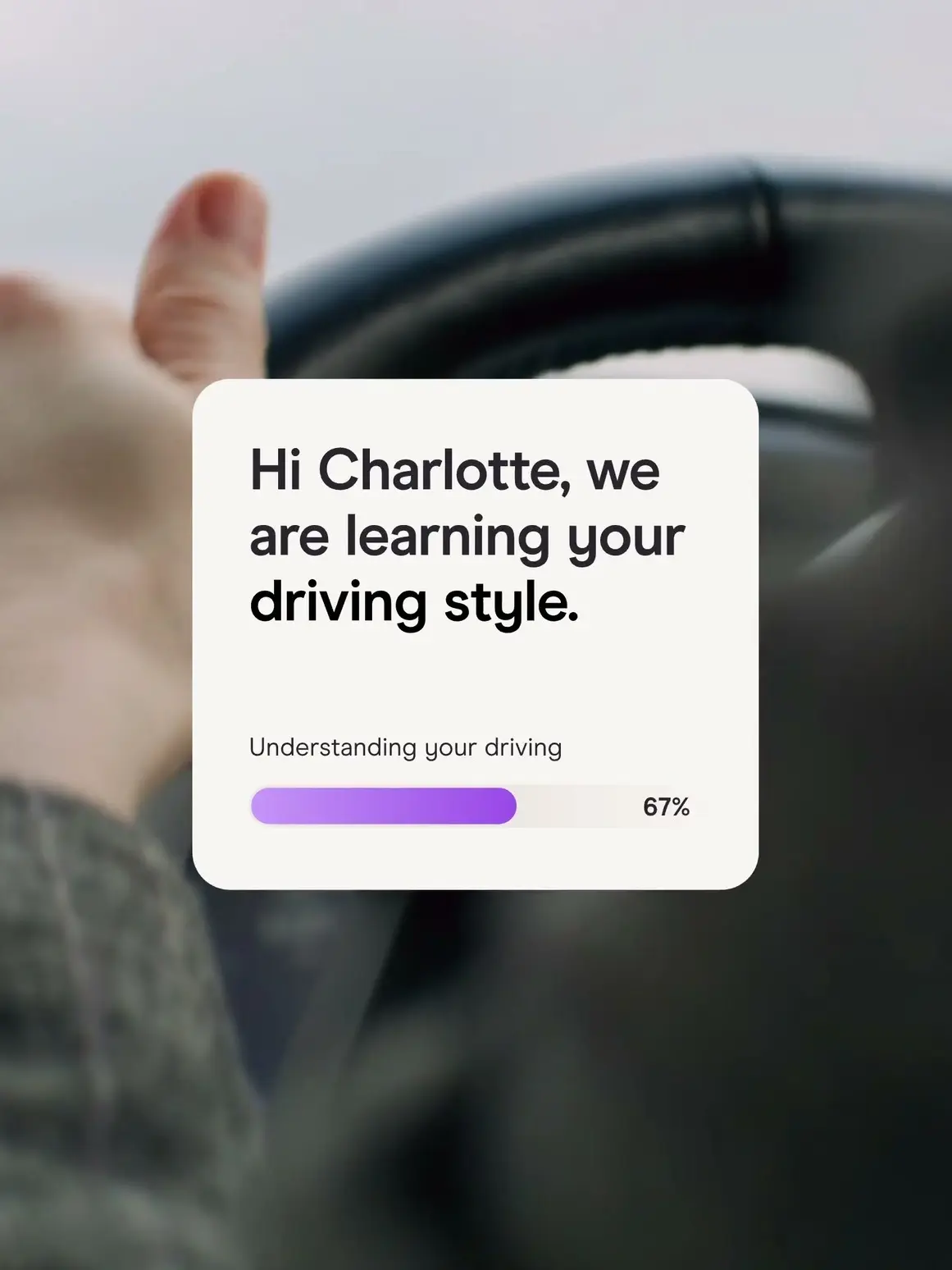 Driver's hand on a steering wheel with an app message, 'Hi Charlotte, we are learning your driving style'